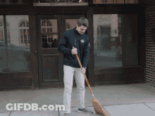 A Man Is Sweeping The Sidewalk In Front Of A Brick Building GIF