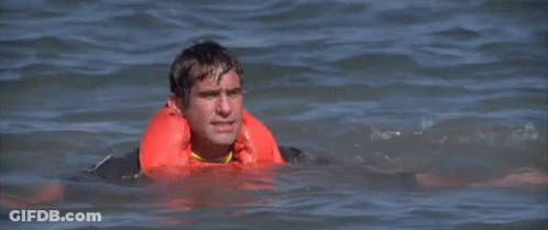A Man Is Swimming In The Ocean Wearing A Life Jacket . GIF