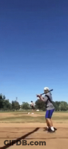 A Man Is Swinging A Bat At A Ball In A Field GIF