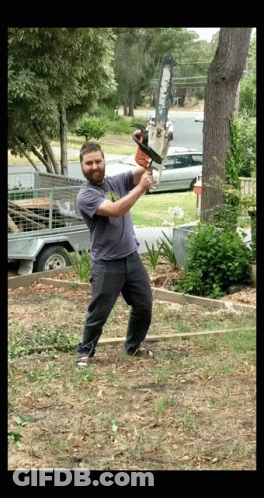 A Man Is Swinging A Chainsaw At A Tree Trunk GIF