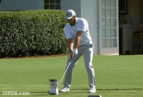 A Man Is Swinging A Golf Club At A Ball On A Golf Course . GIF