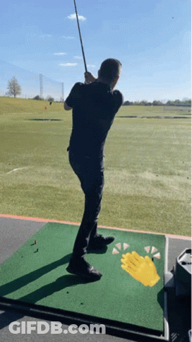 A Man Is Swinging A Golf Club At A Golf Ball GIF
