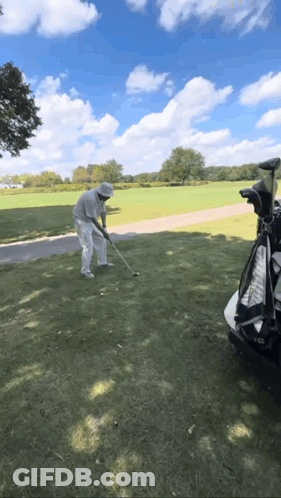 A Man Is Swinging A Golf Club At A Golf Ball GIF