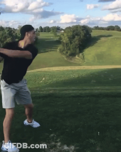 A Man Is Swinging A Golf Club At A Golf Ball GIF