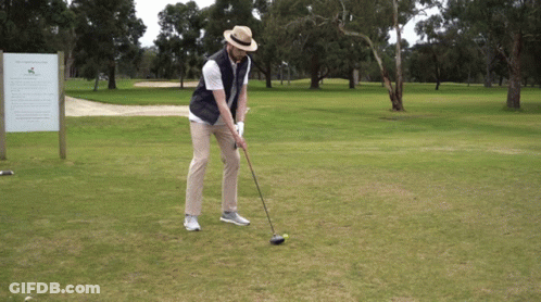 A Man Is Swinging A Golf Club At A Golf Ball On A Golf Course GIF