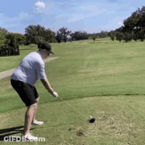 A Man Is Swinging A Golf Club At A Golf Ball On A Golf Course GIF
