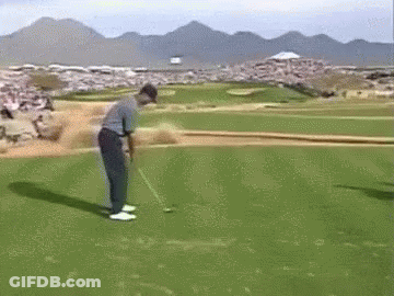 A Man Is Swinging A Golf Club At A Golf Ball On A Golf Course With Mountains In The Background . GIF
