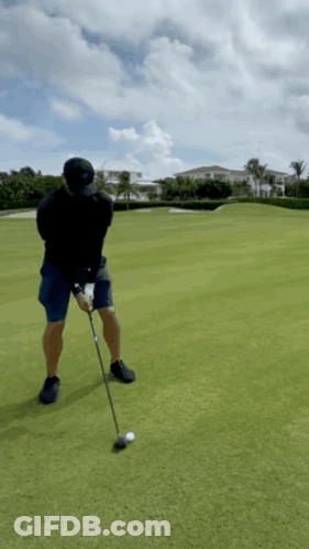 A Man Is Swinging A Golf Club At A Golf Ball On A Golf Course GIF