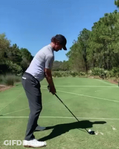 A Man Is Swinging A Golf Club At A Golf Ball On A Green . GIF