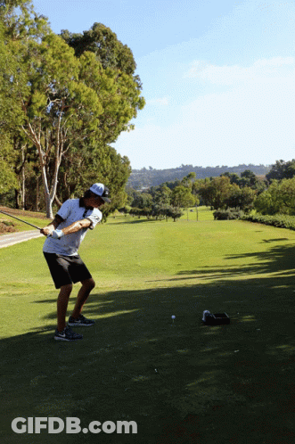 A Man Is Swinging A Golf Club At A Golf Ball GIF