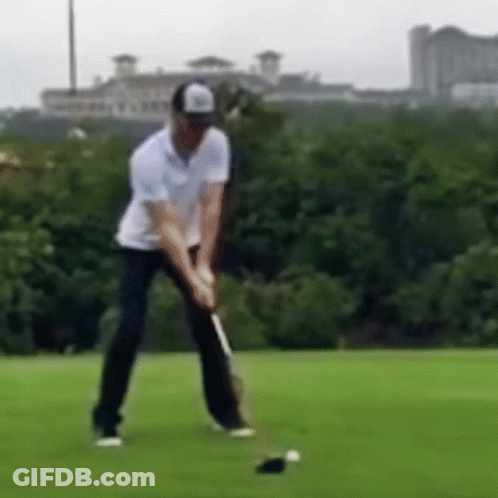 A Man Is Swinging A Golf Club At A Golf Ball . GIF