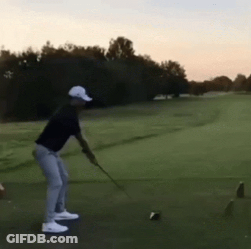 A Man Is Swinging A Golf Club On A Golf Course And Hitting A Ball . GIF