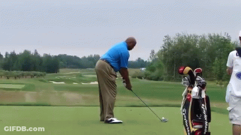 A Man Is Swinging A Golf Club On A Golf Course Next To A Bag That Says Taylormade GIF