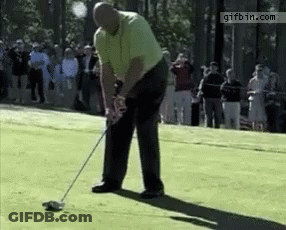 A Man Is Swinging A Golf Club On A Golf Course While A Crowd Watches .. GIF