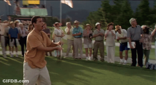 A Man Is Swinging A Golf Club On A Golf Course While A Crowd Watches GIF