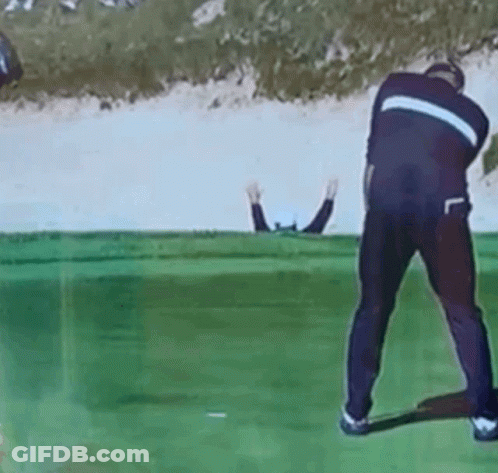 A Man Is Swinging A Golf Club On A Golf Course While Another Man Watches GIF