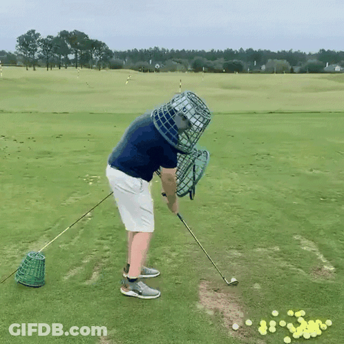 A Man Is Swinging A Golf Club On A Golf Course With A Cage On His Head GIF
