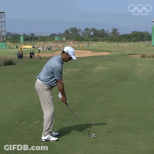 A Man Is Swinging A Golf Club On A Golf Course With The Olympic Rings In The Background GIF