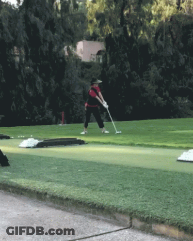 A Man Is Swinging A Golf Club On A Green Course GIF