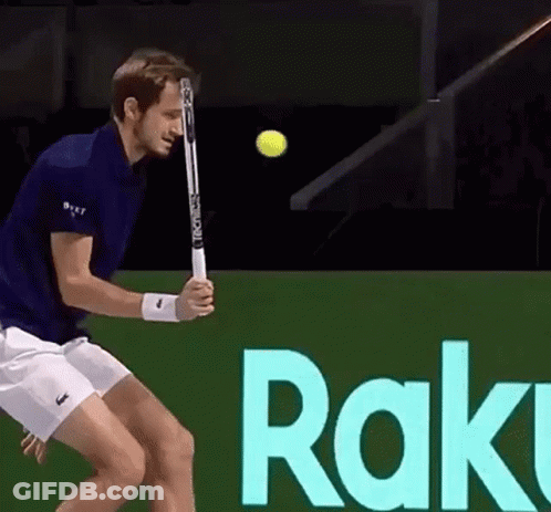 A Man Is Swinging A Tennis Racket At A Tennis Ball In Front Of A Sign That Says Rak GIF
