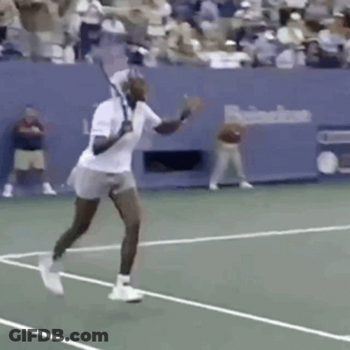 A Man Is Swinging A Tennis Racket On A Tennis Court In Front Of A Crowd . GIF
