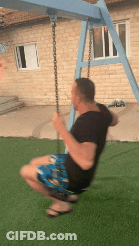A Man Is Swinging On A Blue Swing Set In Front Of A Brick Building GIF