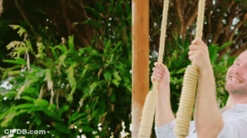 A Man Is Swinging On A Rope Swing Outside GIF