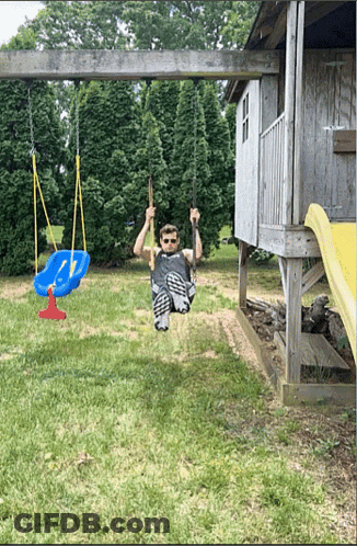 A Man Is Swinging On A Swing Set In A Yard GIF