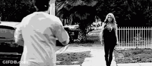 A Man Is Taking A Picture Of A Woman Walking Down The Street . GIF