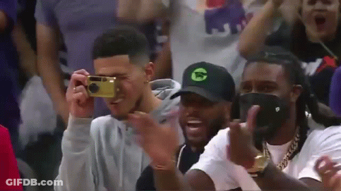 A Man Is Taking A Picture Of Another Man With A Camera While Sitting In The Stands . GIF