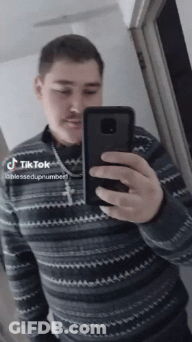 A Man Is Taking A Picture Of Himself In A Mirror With A Cross Necklace On His Neck GIF