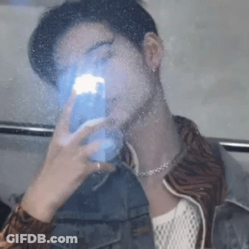 A Man Is Taking A Picture Of Himself In A Mirror With His Phone . GIF