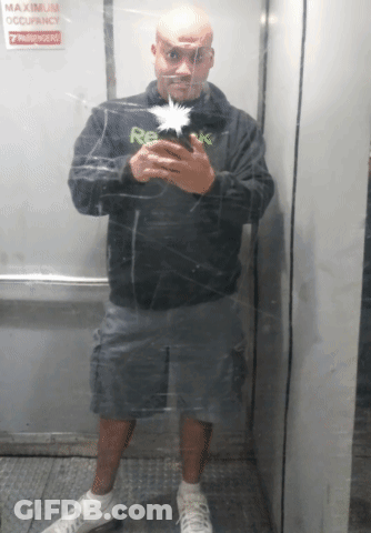 A Man Is Taking A Picture Of Himself In An Elevator With A Sign That Says Maximum Occupancy 7 Passengers GIF