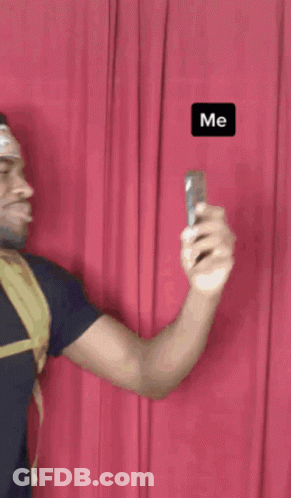 A Man Is Taking A Picture Of Himself With A Red Curtain Behind Him And The Word Me Is On The Bottom Right GIF