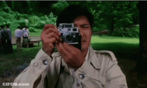 A Man Is Taking A Picture With A Camera In The Park . GIF