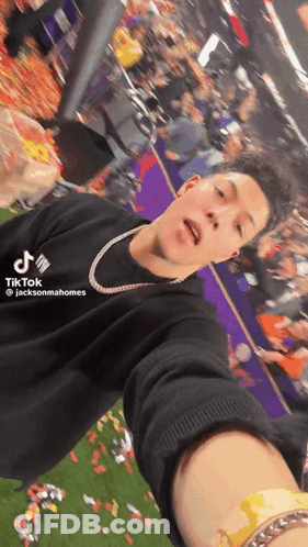 A Man Is Taking A Selfie In Front Of A Crowd While Wearing A Black Shirt That Says Tiktok GIF