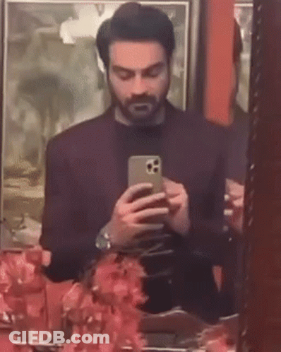 A Man Is Taking A Selfie In Front Of A Mirror While Looking At His Phone . GIF