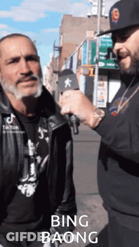 A Man Is Talking Into A Microphone While Another Man Looks On And Says Bing Baong GIF