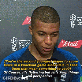A Man Is Talking Into A Microphone While Standing In Front Of A Wall That Says Bud On It . GIF