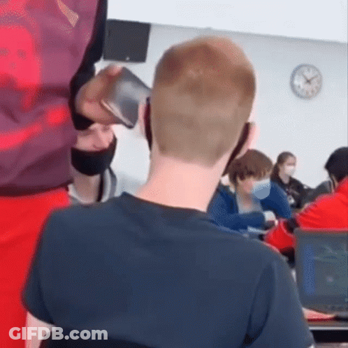A Man Is Talking On A Cell Phone In A Classroom While Sitting At A Desk . GIF