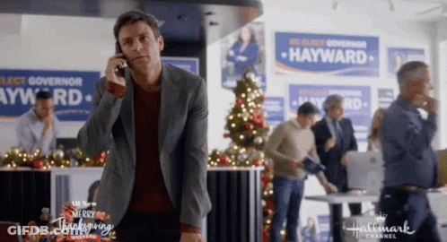 A Man Is Talking On A Cell Phone In Front Of A Hallmark Channel Ad For Hayward . GIF