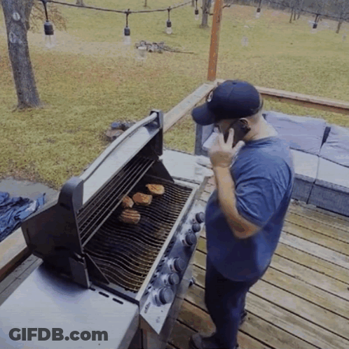 A Man Is Talking On A Cell Phone While Grilling GIF