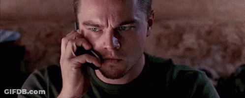 A Man Is Talking On A Cell Phone While Looking At Something . GIF