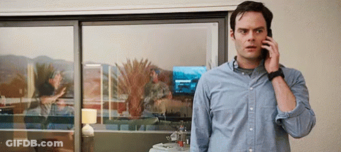 A Man Is Talking On A Cell Phone While Standing In Front Of A Sliding Glass Door . GIF