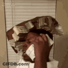 A Man Is Talking On A Cell Phone While Wearing A Hat Made Of Money . GIF