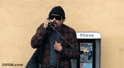 A Man Is Talking On A Pay Phone Next To A Phone Booth . GIF
