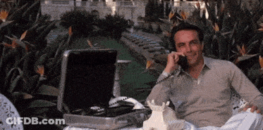 A Man Is Talking On A Phone In Front Of A Briefcase GIF