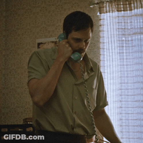 A Man Is Talking On A Telephone In Front Of A Window GIF