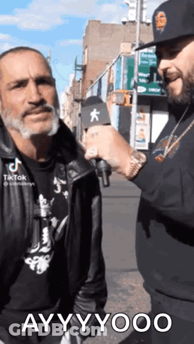 A Man Is Talking To A Homeless Man With A Microphone On The Street . GIF