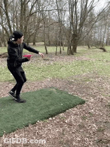 A Man Is Throwing A Frisbee On A Frisbee Course In The Woods . GIF